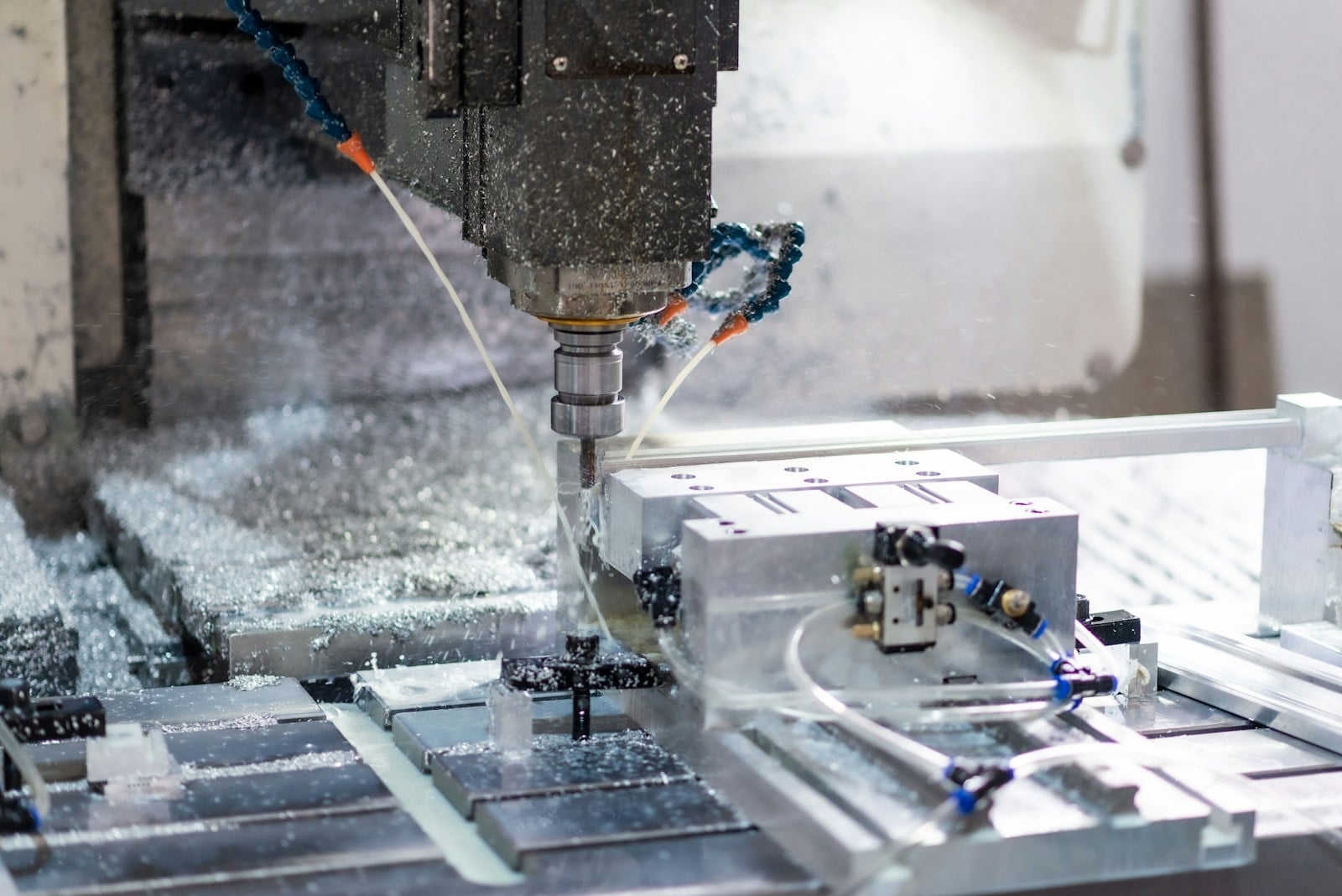 A CNC vertical machining center cutting an aluminum fixture, with coolant and machined chips visible around the spindle